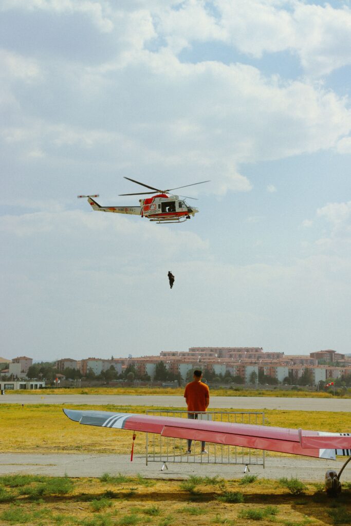 A helicopter performs training exercises over an airfield while a man observes from the ground.