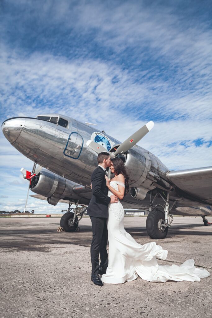 Bride and groom embrace by a vintage airplane in Melbourne, capturing timeless wedding memories.